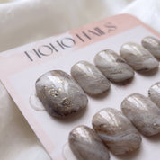 Close-up of Sediment No. 9 press-on nails by Noho Nails: hand-painted swirls of greige, warm taupe and chalky white with gold flecks