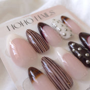 Close-up of Noir et Crème press-on nails by Noho Nails: long almond nails with cream and black-cherry French tips, brown pinstripes, tortoiseshell tips and silver studs