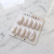 Prosecco Pearl press-on nails on a Noho Nails display card lying on white marble