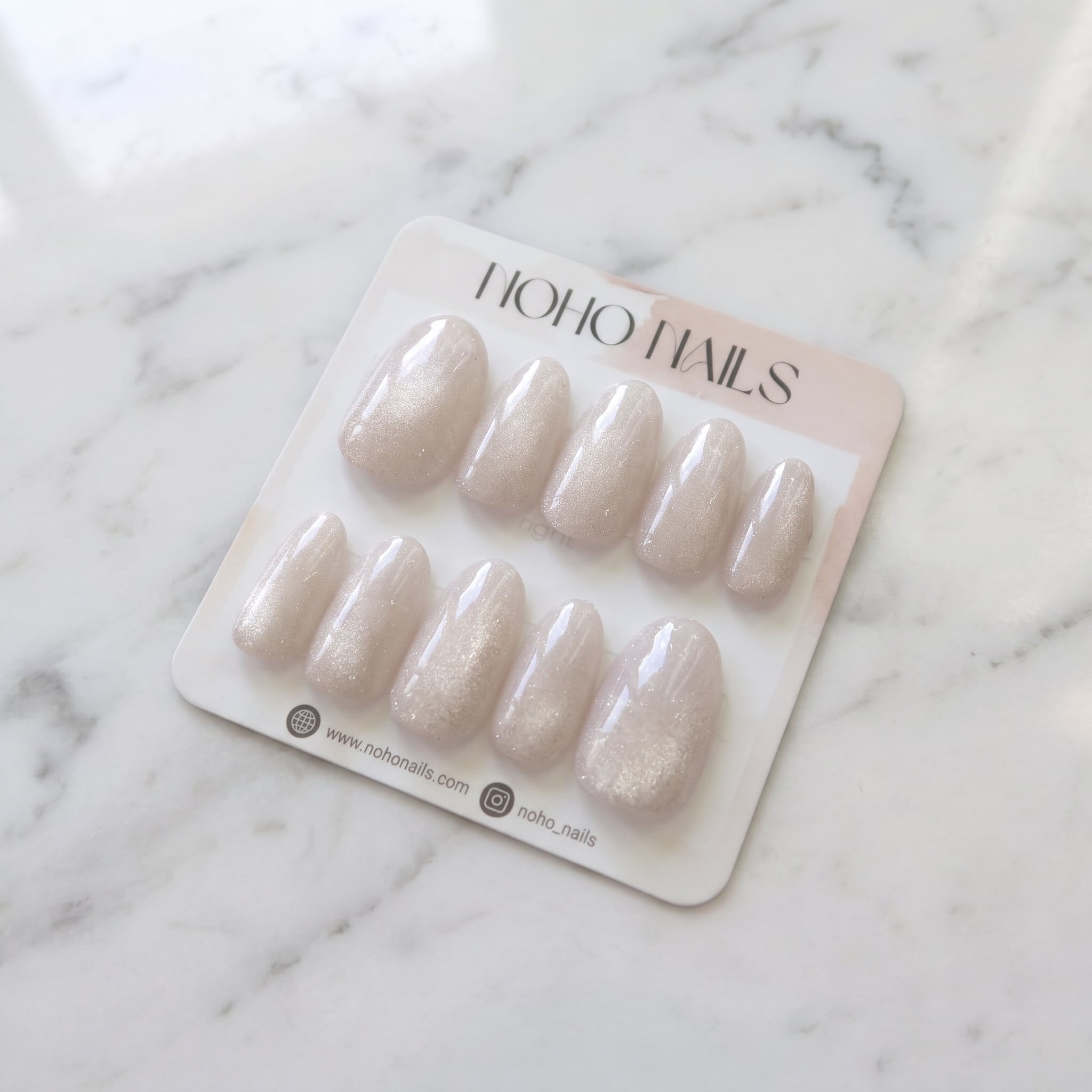 Prosecco Pearl press-on nails on a Noho Nails display card lying on white marble