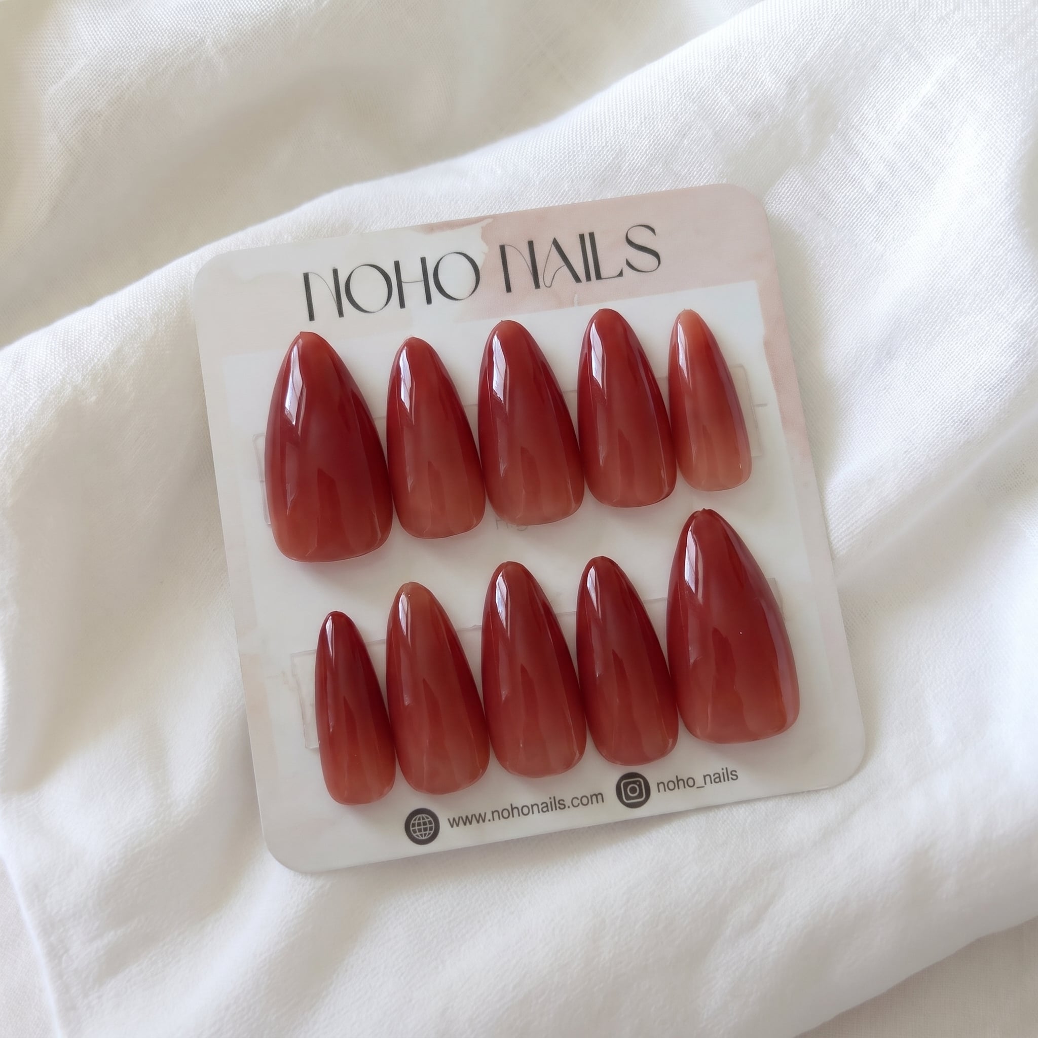 Overdone press-on nails by Noho Nails: ten long stiletto nails in a brick red jelly ombre on a Noho Nails display card