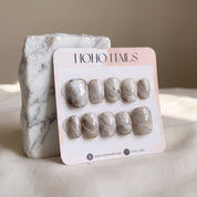 Sediment No. 9 press-on nails on a Noho Nails display card propped against a white marble stone