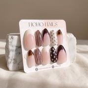 Noir et Crème press-on nails on a Noho Nails display card propped against a white marble stone