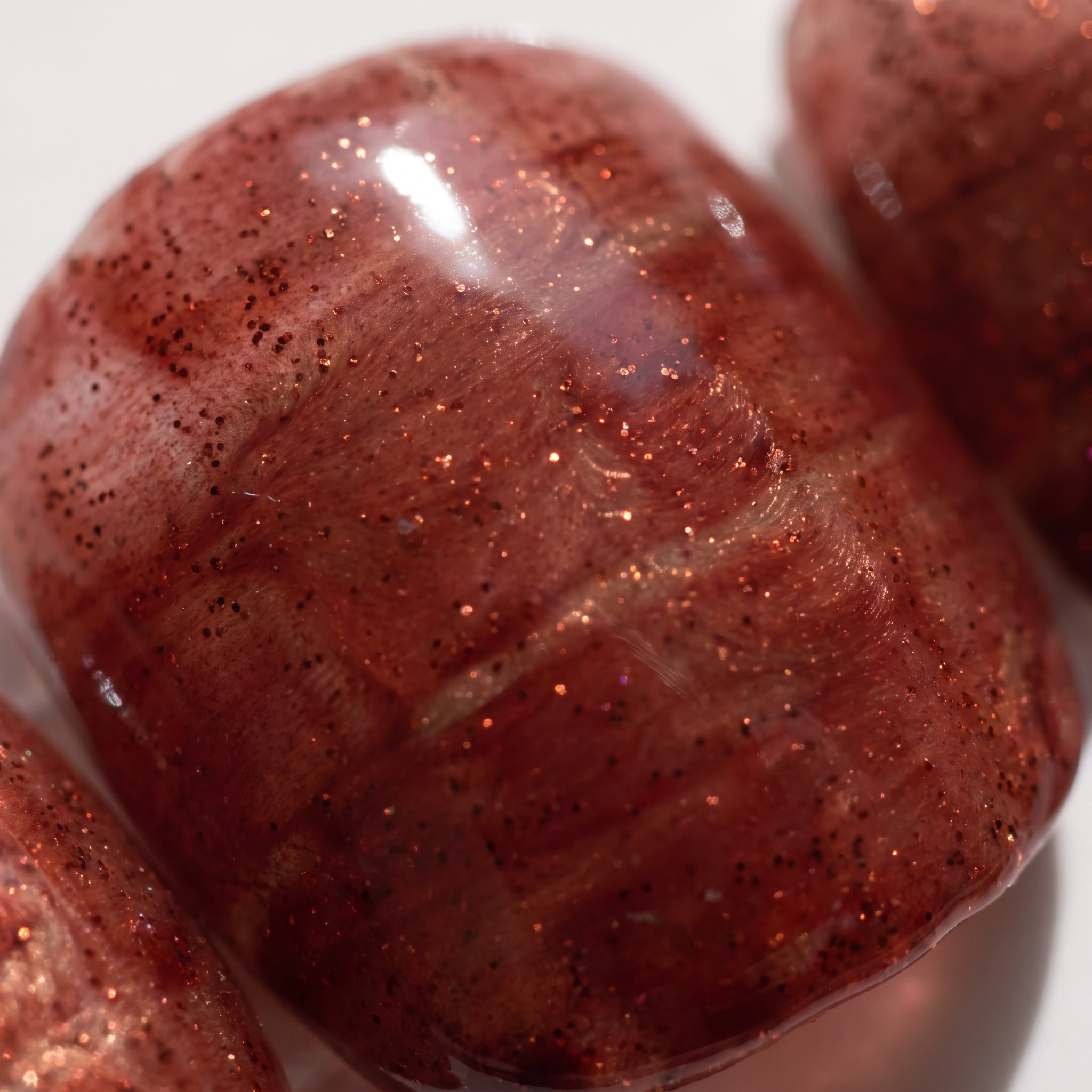 Macro close-up of a Cognac Emboss press-on nail showing the glossy cognac finish, streaked texture and copper glitter