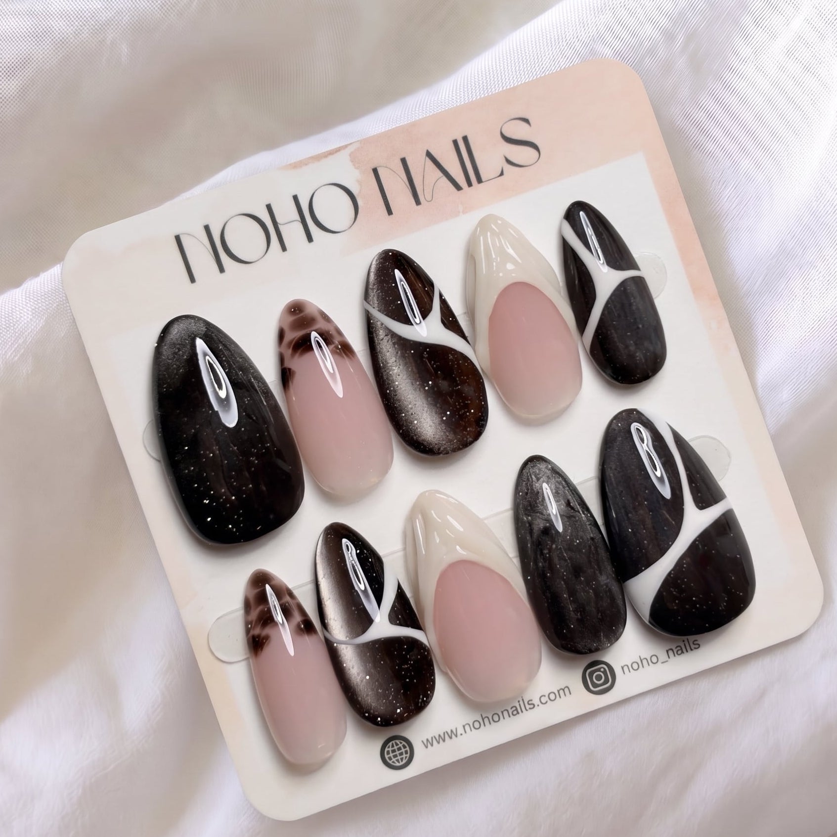 Café de Flore press-on nails by Noho Nails: long almond nails in dark brown cat-eye glitter with white line art, tortoiseshell tips and cream French tips on a Noho Nails display card