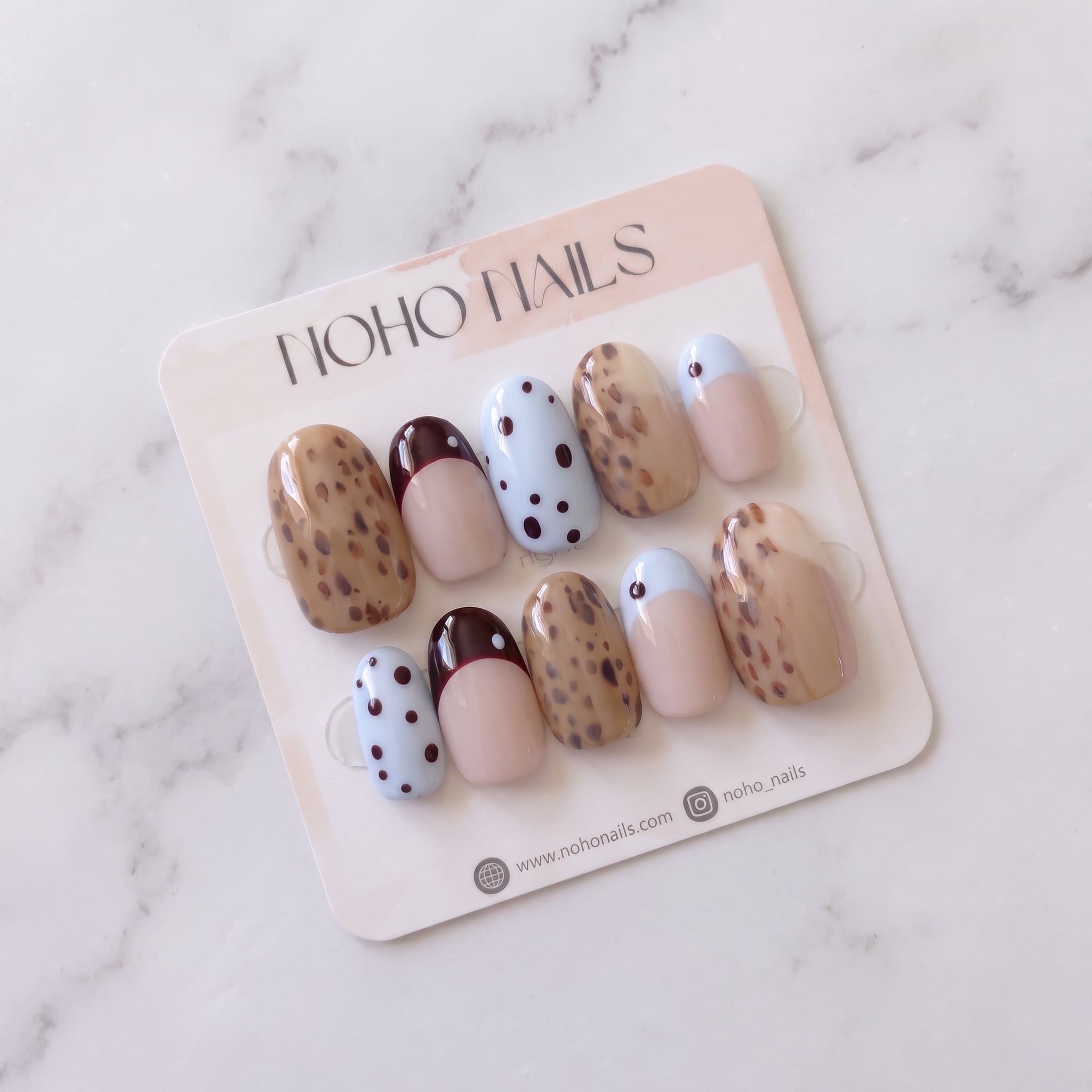 Petite Tache press-on nails on a Noho Nails display card lying on white marble