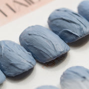 Macro close-up of Slate Relief press-on nails by Noho Nails showing the hand-sculpted ridges and swept grooves in matte dusty blue-gray