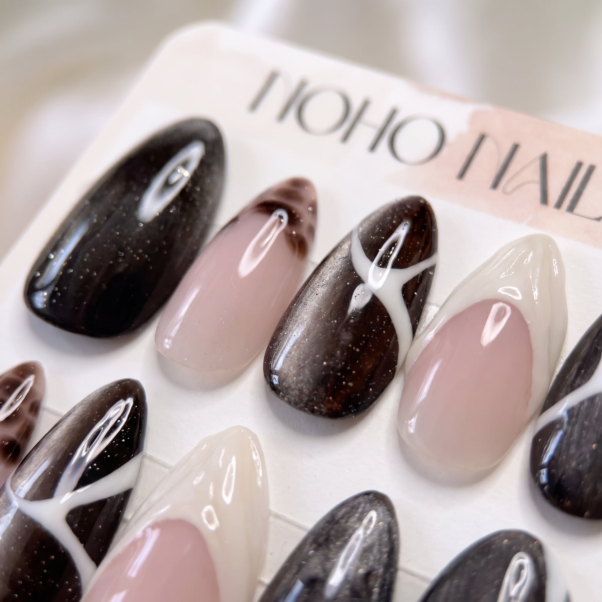 Close-up of Café de Flore press-on nails by Noho Nails: long almond nails in dark brown cat-eye glitter with white line art, tortoiseshell tips and cream French tips