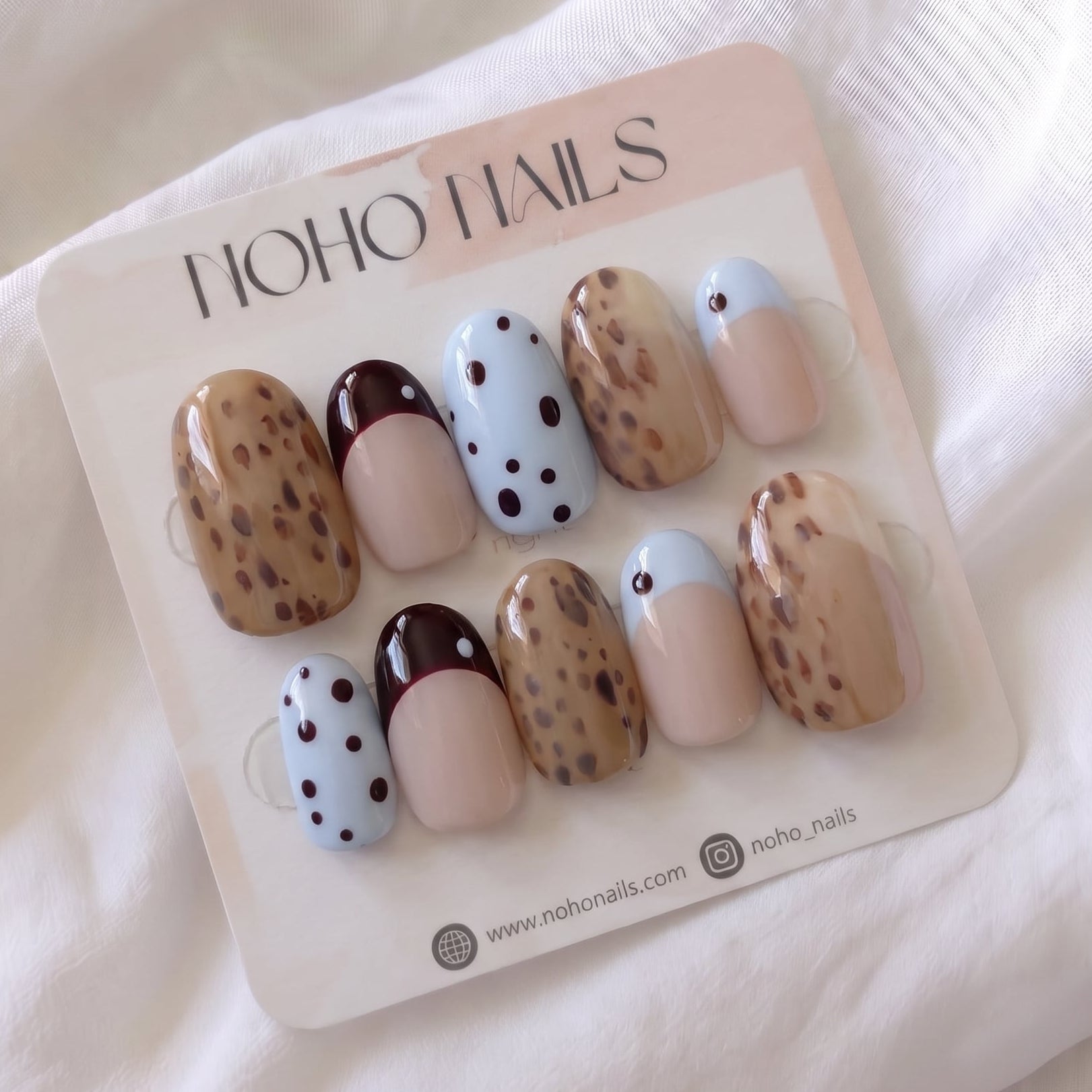 Petite Tache press-on nails by Noho Nails: short round nails with caramel leopard spots, baby-blue polka dots, and black-cherry and baby-blue French tips on a Noho Nails display card