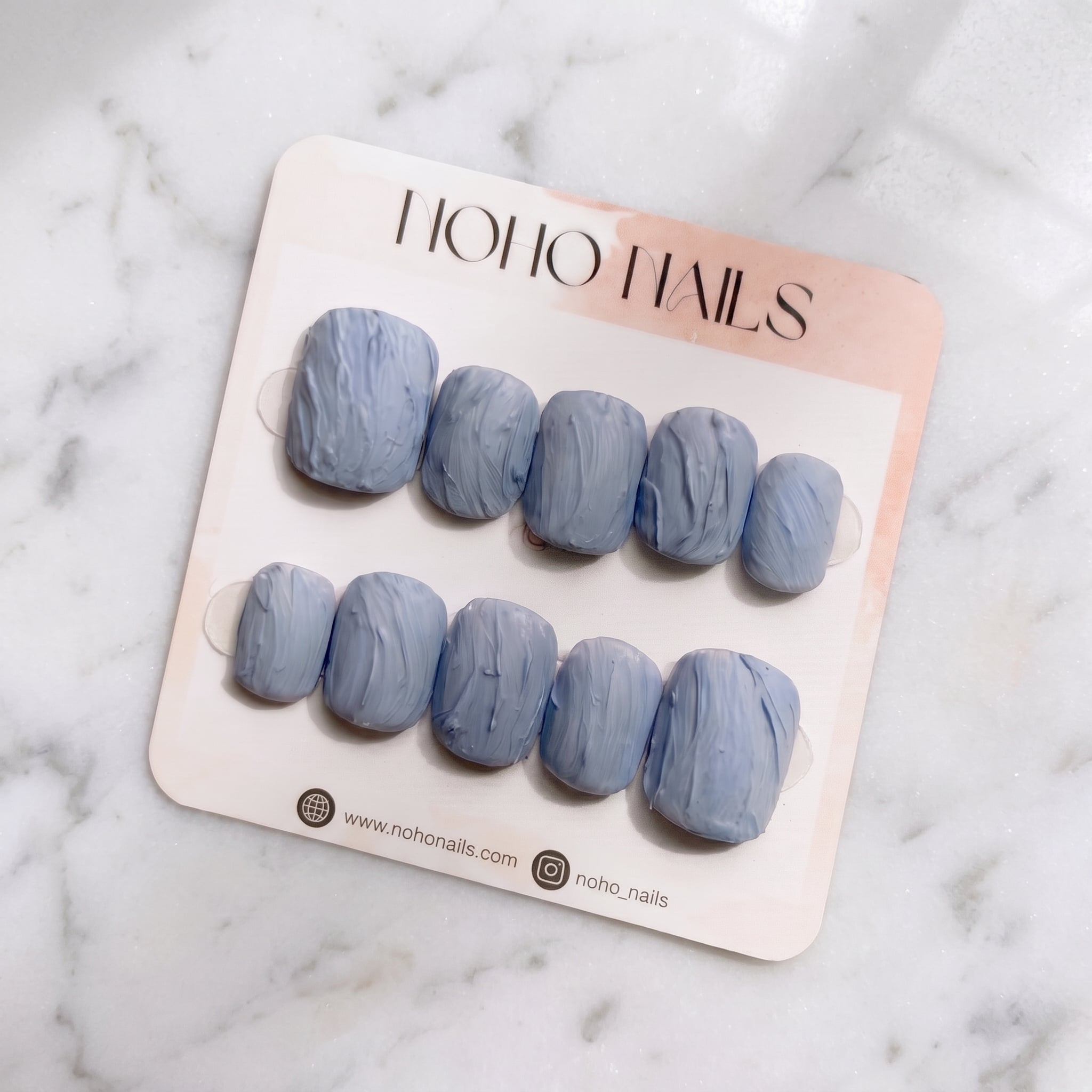 Slate Relief press-on nails on a Noho Nails display card lying on white marble