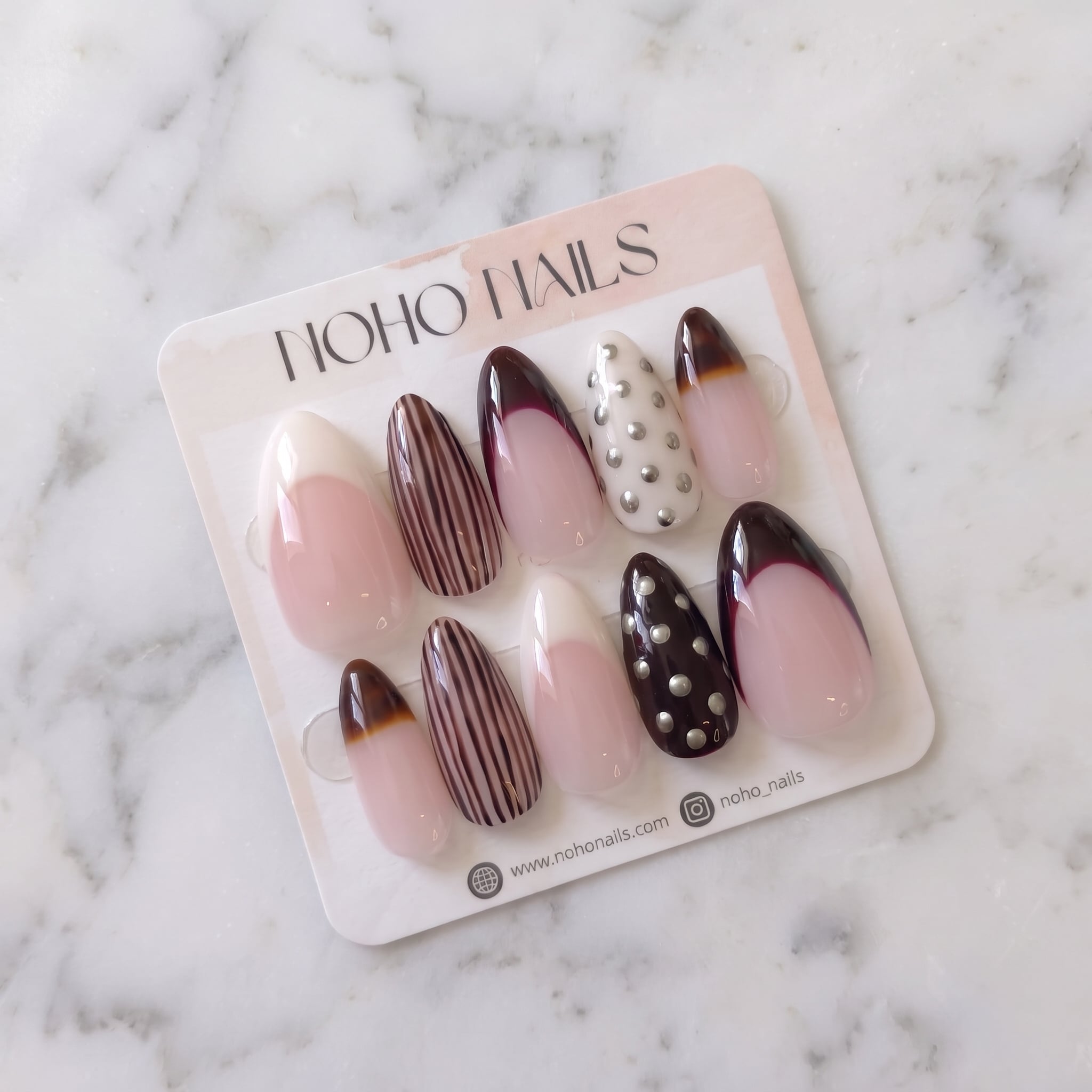 Noir et Crème press-on nails on a Noho Nails display card lying on white marble