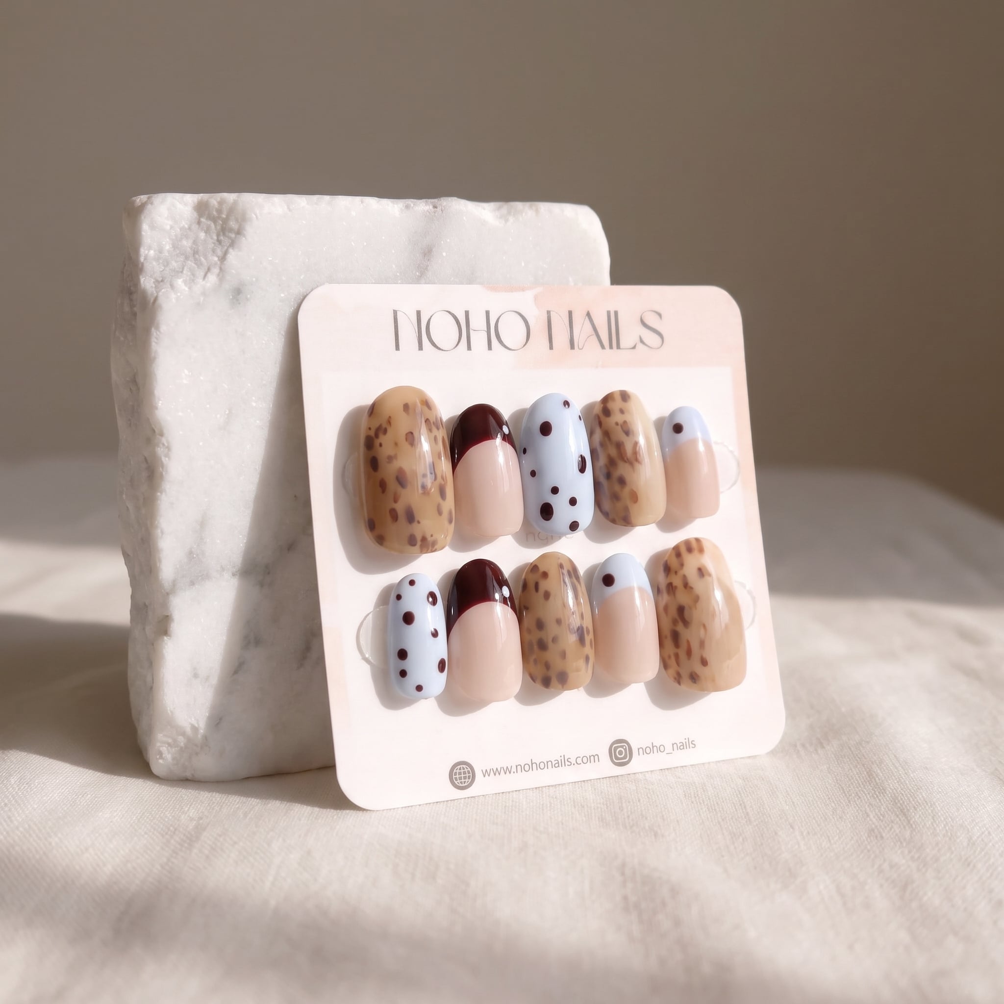 Petite Tache press-on nails on a Noho Nails display card propped against a white marble stone