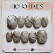 Sediment No. 9 press-on nails by Noho Nails: ten short squoval nails with hand-painted greige, taupe and chalky white swirls, gold flecks and a faceted finish on a display card