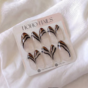 Ombre Portée press-on nails by Noho Nails: long almond nails with a sheer clear base, chocolate-brown tips and wavy caramel and black stripes on a Noho Nails display card