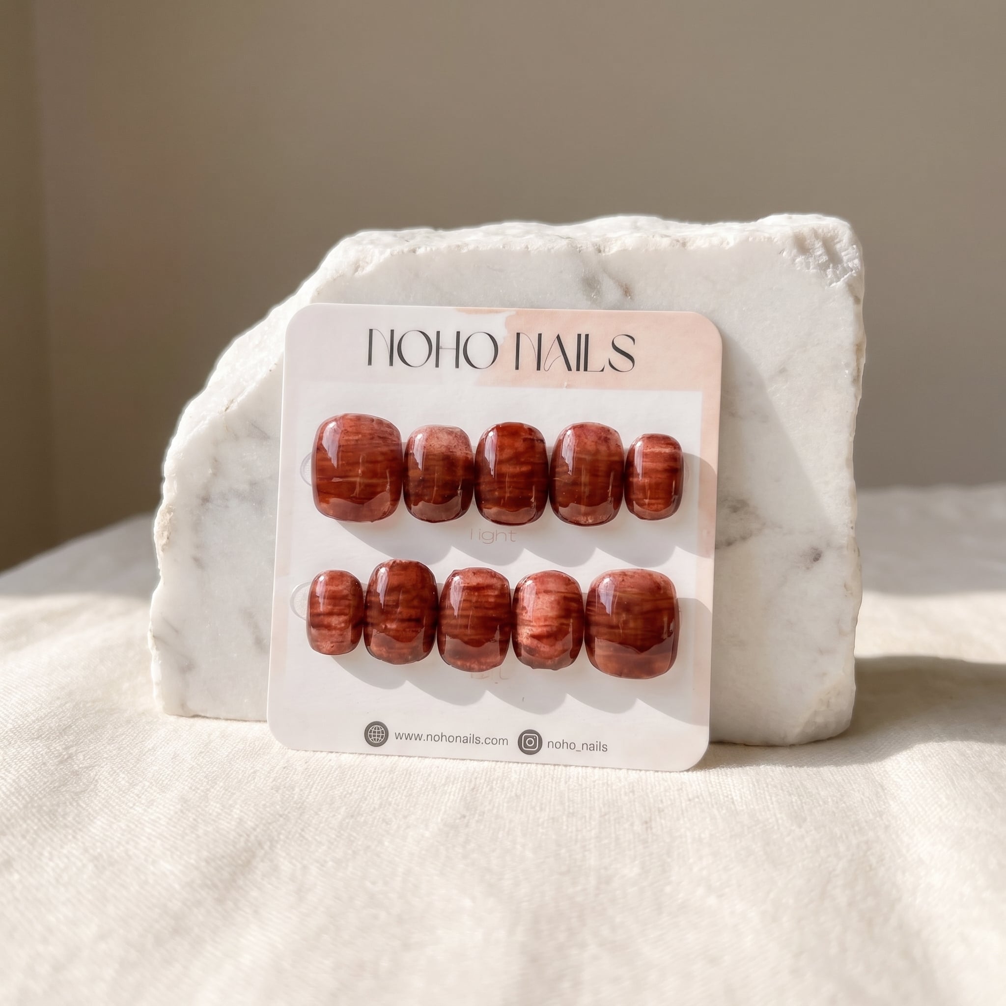 Cognac Emboss press-on nails on a Noho Nails display card propped against a white marble stone