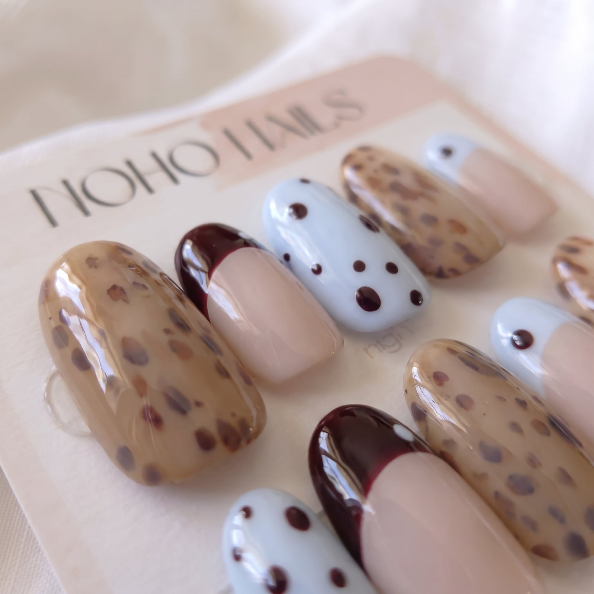 Close-up of Petite Tache press-on nails by Noho Nails: short round nails with caramel leopard spots, baby-blue polka dots and black-cherry and baby-blue French tips