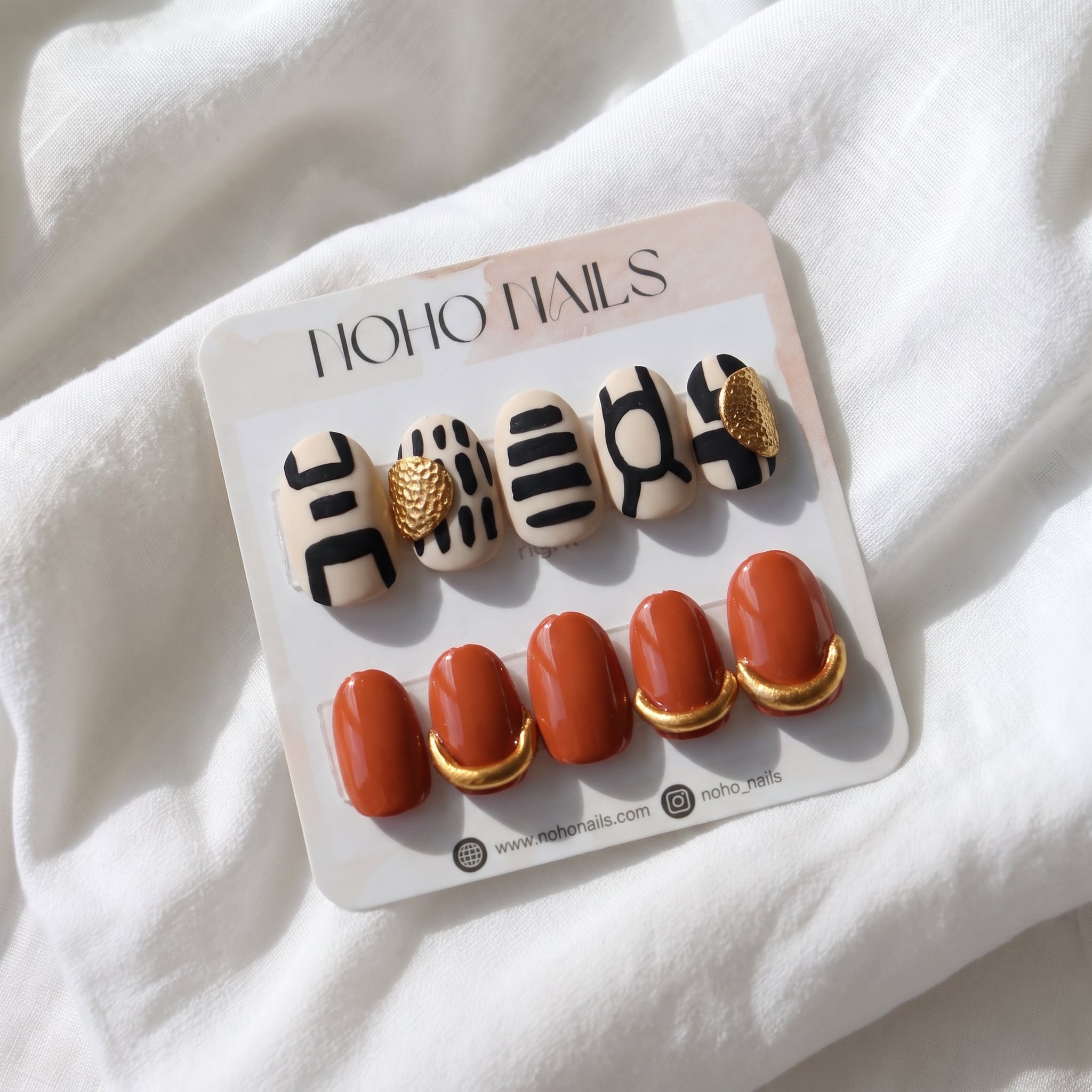 Out of Africa press-on nails by Noho Nails: cream nails with black abstract lines and terracotta nails with gold cuffs on a Noho Nails display card