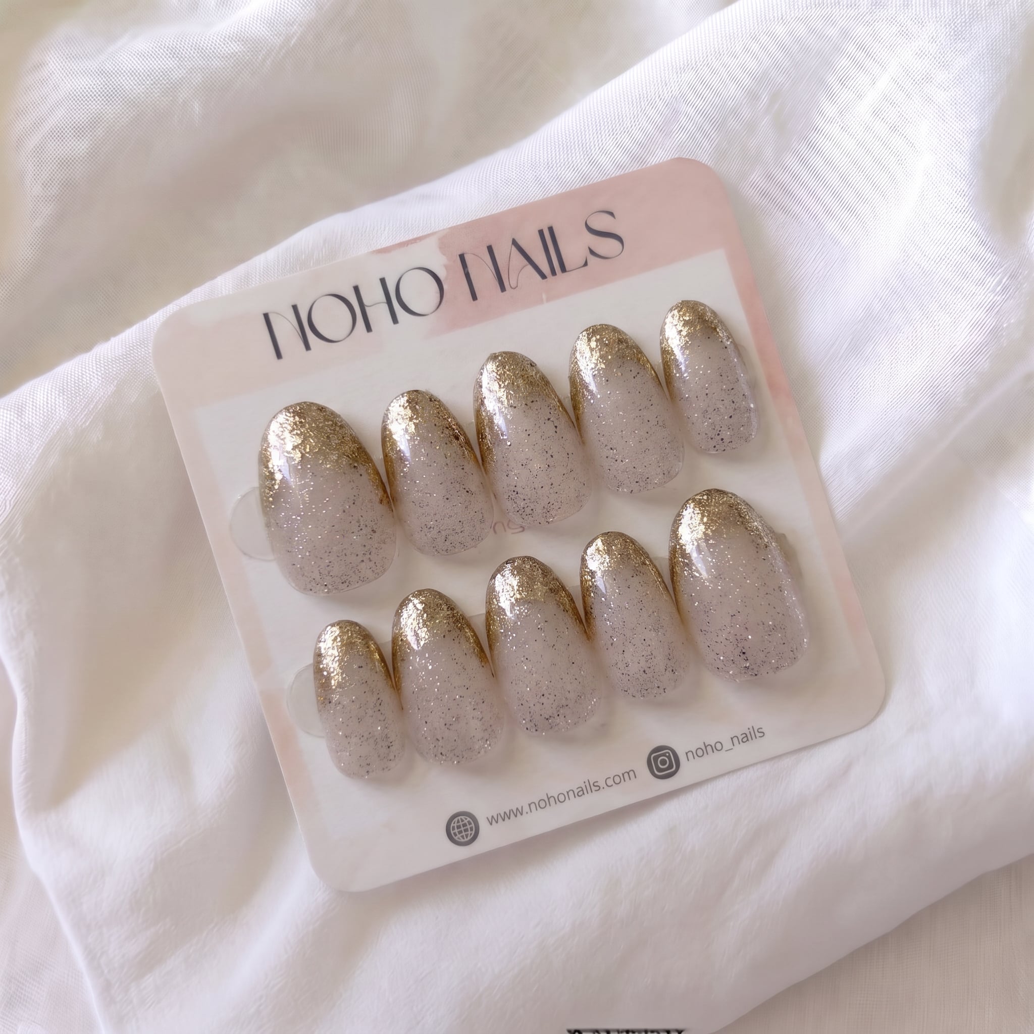 Golden Glaze press-on nails by Noho Nails: ten oval nails in sheer nude with speckled glitter and gold glitter tips on a Noho Nails display card