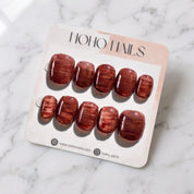 Cognac Emboss press-on nails on a Noho Nails display card lying on white marble