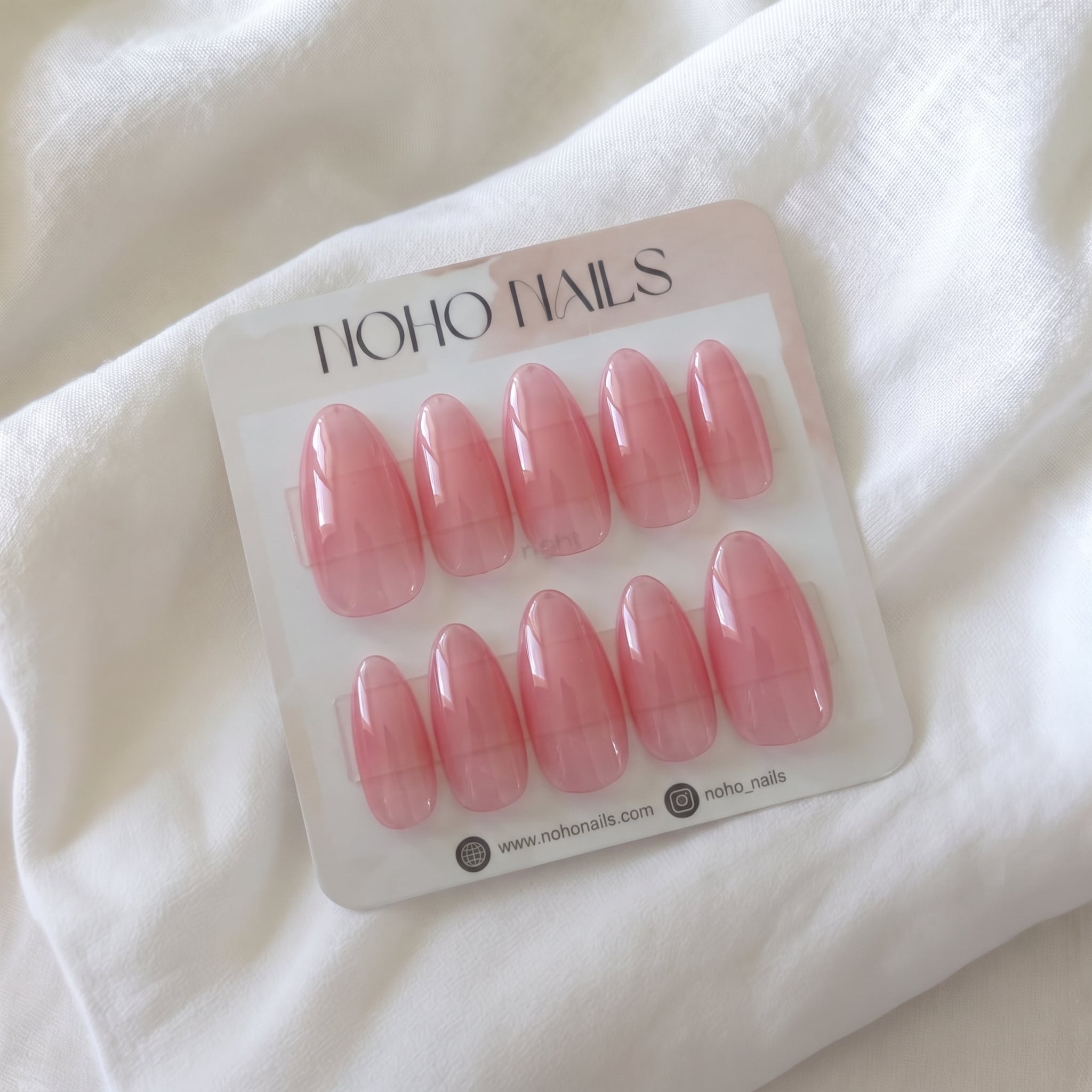Flushed press-on nails by Noho Nails: ten long almond nails in sheer glossy pink jelly on a Noho Nails display card