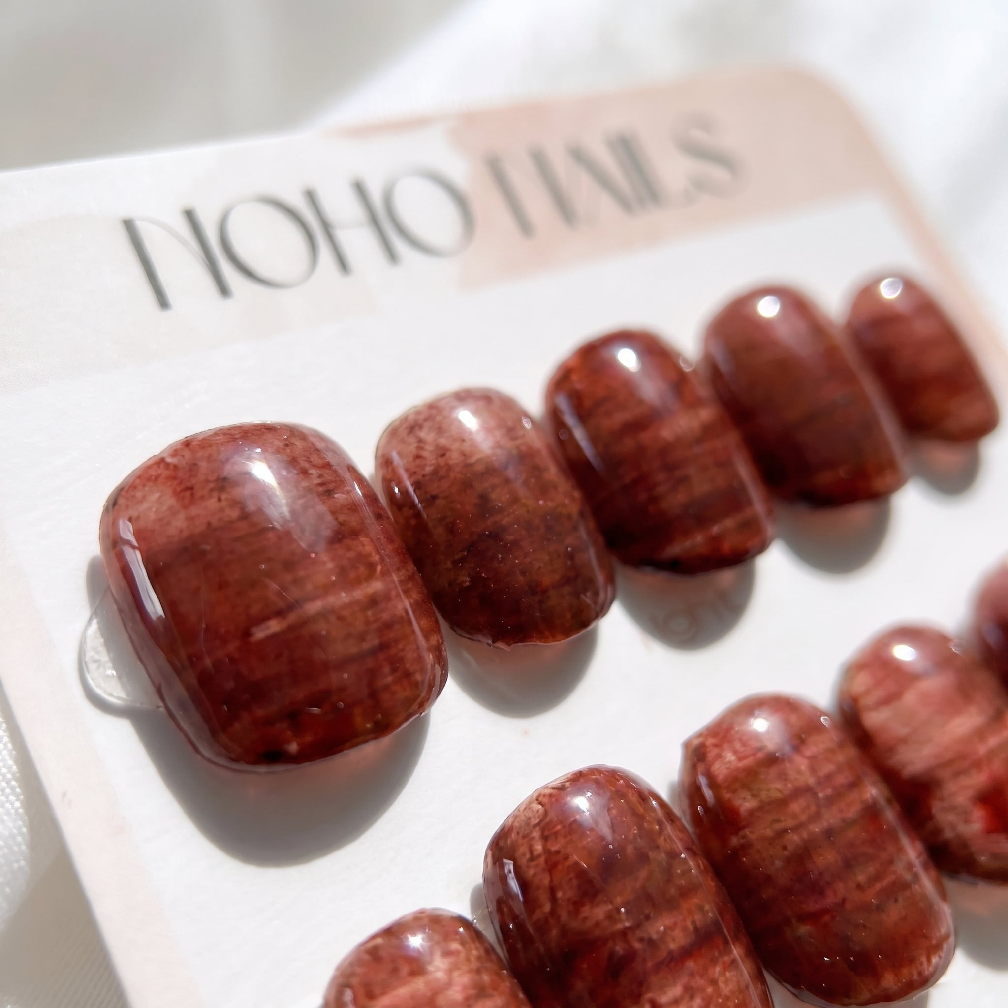 Close-up of Cognac Emboss press-on nails by Noho Nails: glossy deep cognac and copper nails with a streaked, embossed texture