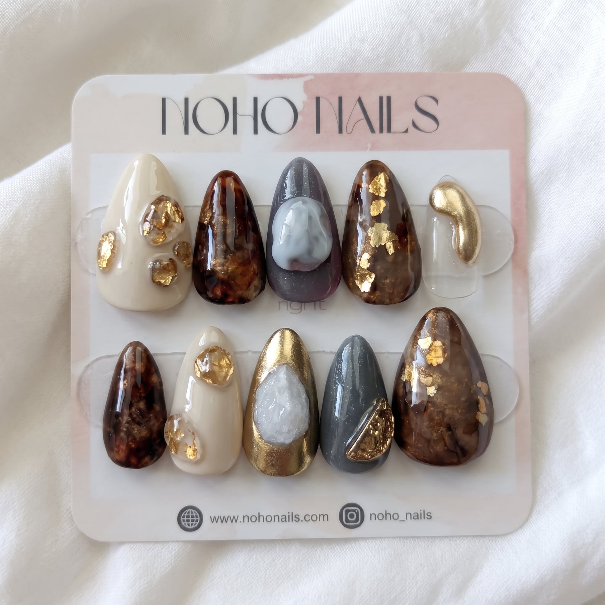 Gilded Earth press-on nails by Noho Nails: long almond nails in cream, tortoiseshell, slate gray and gold with gold flakes on a Noho Nails display card
