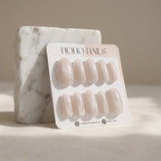 Prosecco Pearl press-on nails on a Noho Nails display card propped against a white marble stone