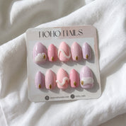 Pastel Skies press-on nails by Noho Nails: pastel pink and lilac almond nails with white 3D swirls and gold studs on a Noho Nails display card