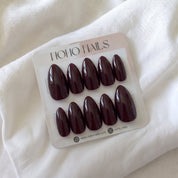 Blood Moon press-on nails by Noho Nails: ten glossy deep black-cherry stiletto nails on a Noho Nails display card