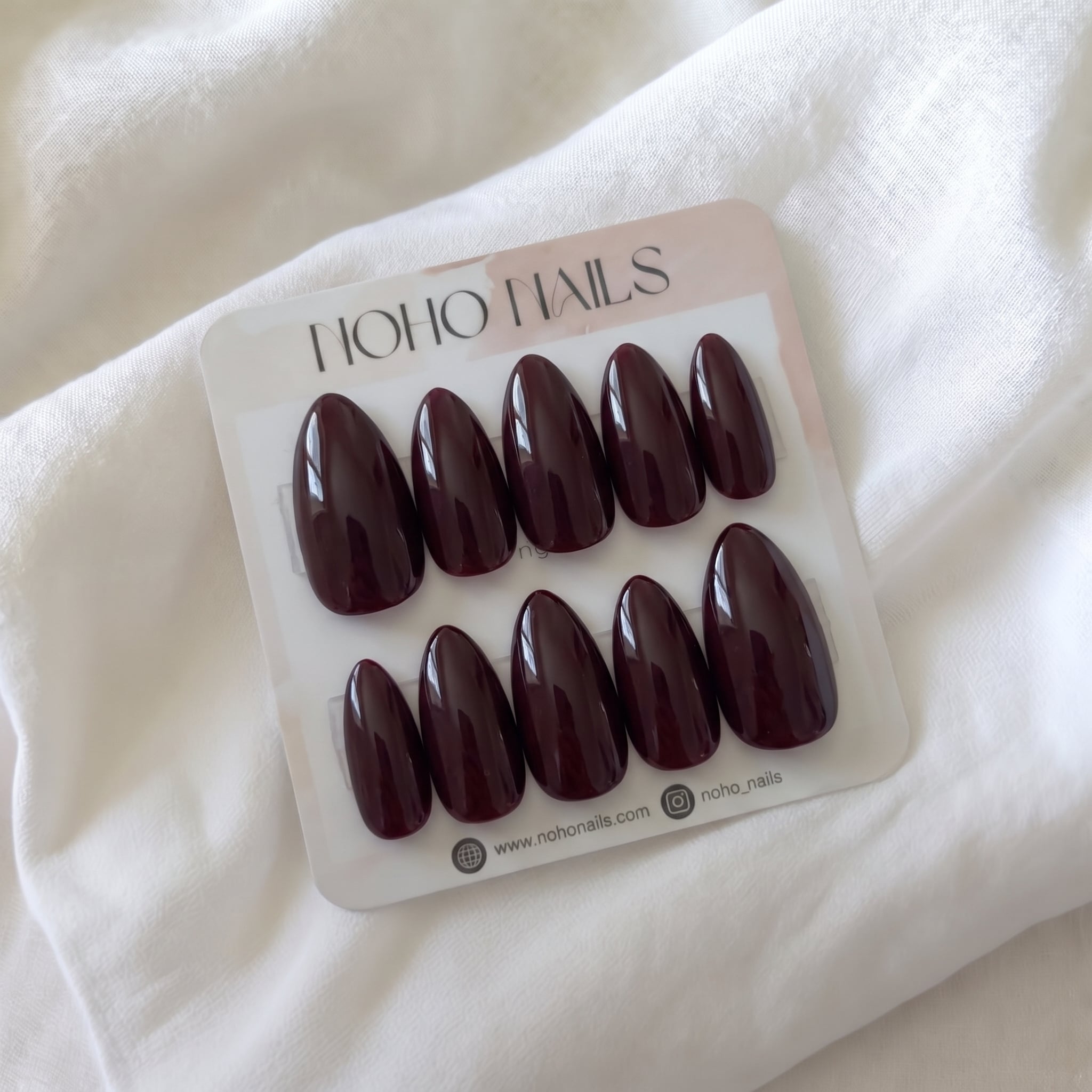Blood Moon press-on nails by Noho Nails: ten glossy deep black-cherry stiletto nails on a Noho Nails display card